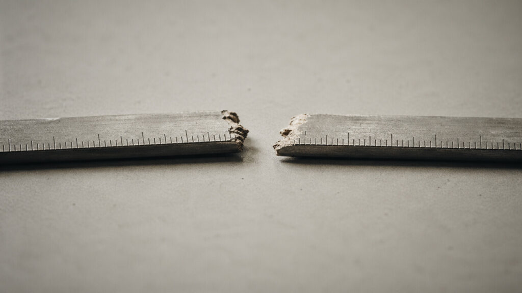 A wooden ruler snapped in two, photographed on a grey surface — illustrating the broken inflation measurement framework facing the incoming Federal Reserve Chair.