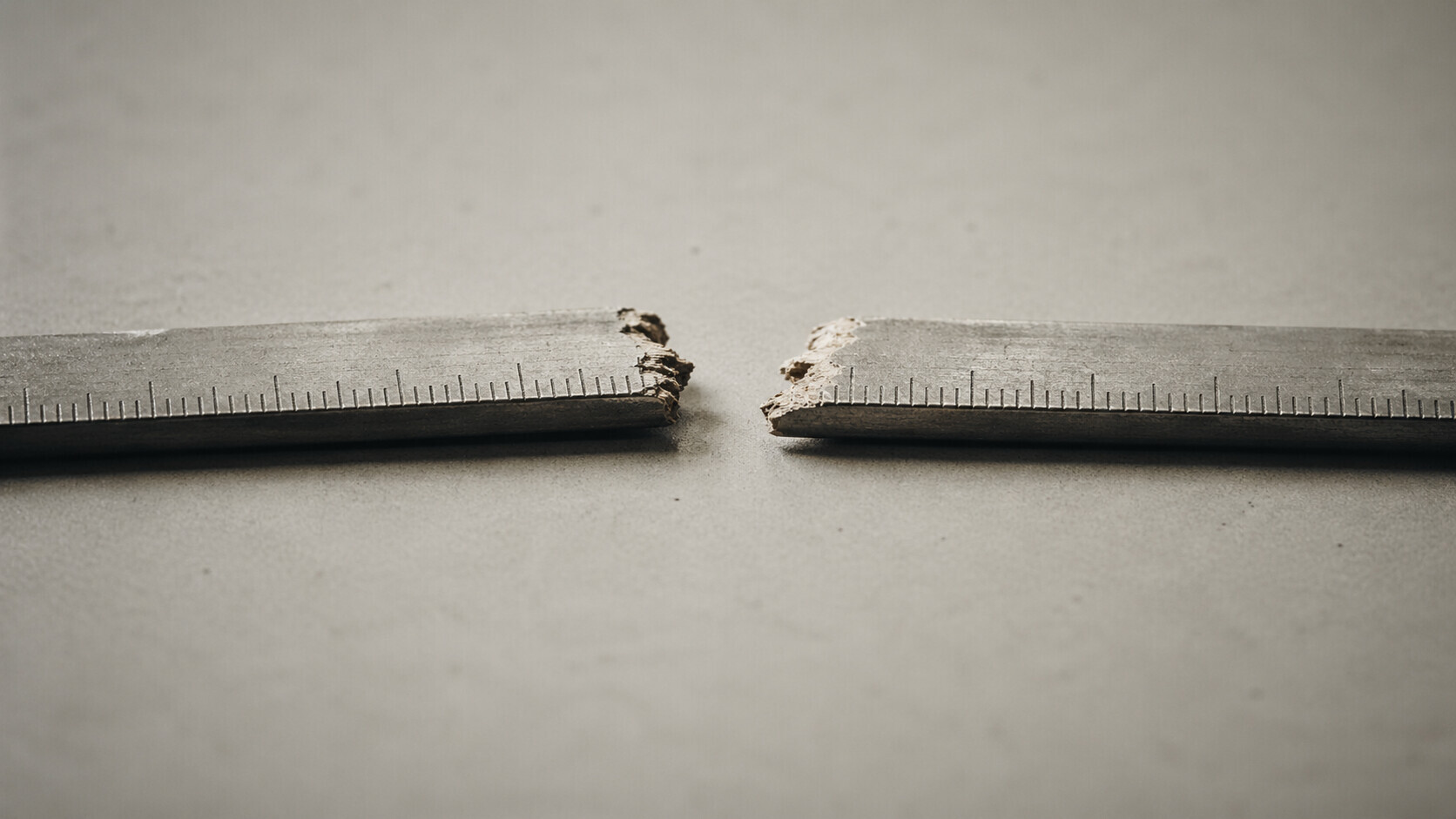 A wooden ruler snapped in two, photographed on a grey surface — illustrating the broken inflation measurement framework facing the incoming Federal Reserve Chair.