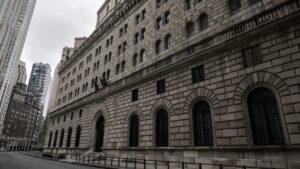 Exterior of the Federal Reserve Bank of New York building on Liberty Street, Manhattan, showing the neoclassical stone facade, arched windows, and surrounding skyscrapers under an overcast sky.