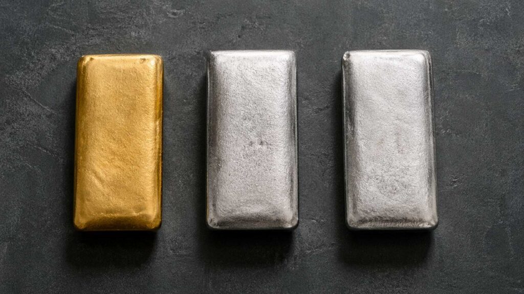 One gold bar and two silver bars on a dark stone surface