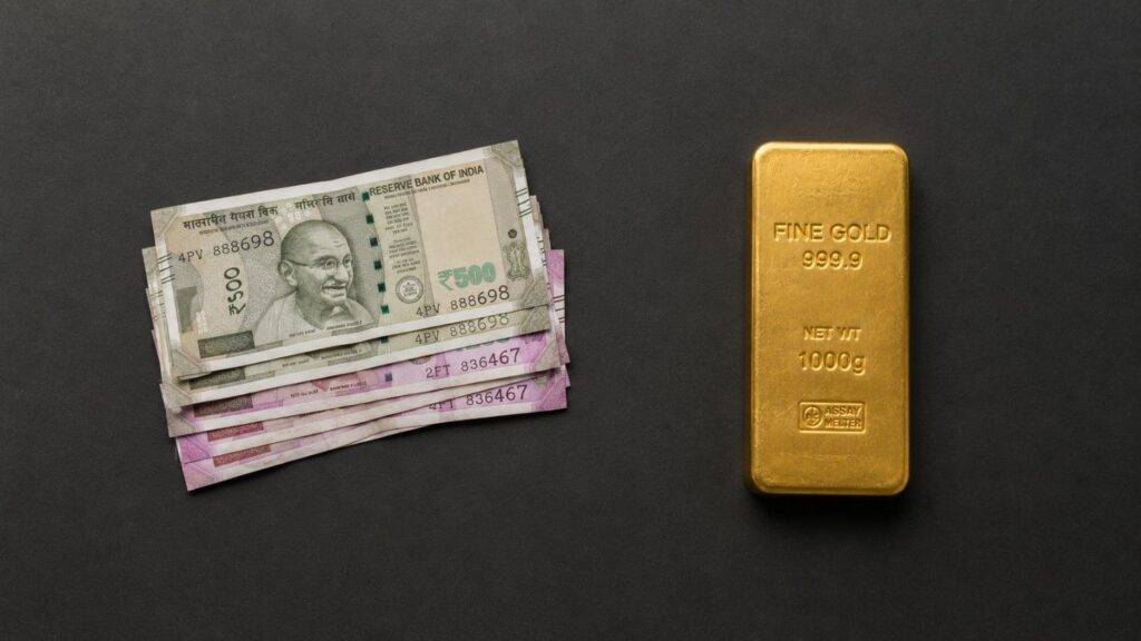 Indian rupee banknotes beside a 1000g fine gold bullion bar on a dark surface — illustrating India's gold import duty hike and the rupee vs gold tension