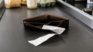 Empty wallet with receipt on grocery store conveyor belt — economic warning signs for gold investors as savings rates hit multi-year lows