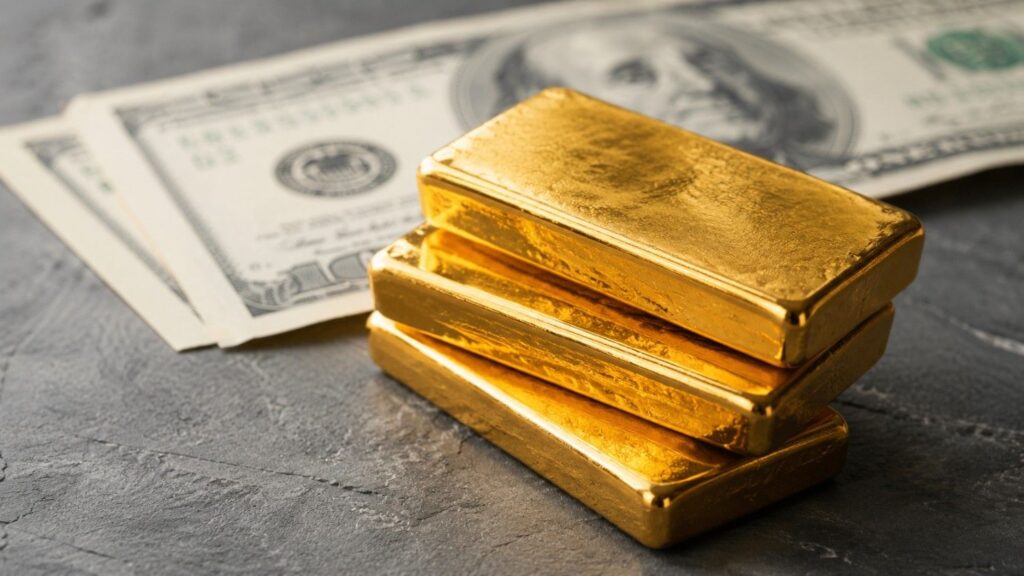 Three stacked gold bars on a dark slate surface with US dollar bills fanned out in soft focus behind them, illustrating the inverse gold dollar relationship.