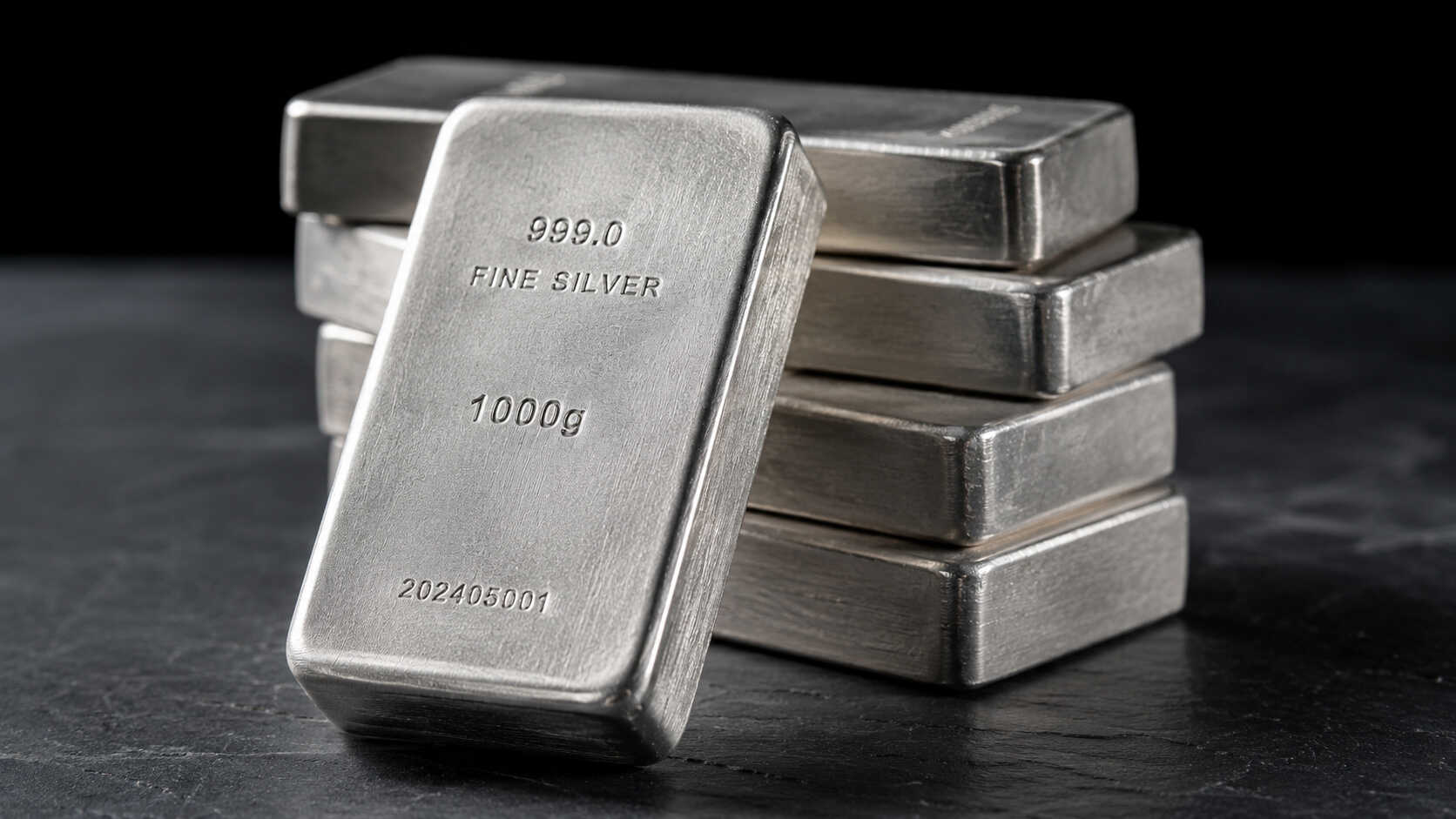 Stack of 999.0 fine silver bullion bars on a dark slate surface, illustrating physical silver as a long-term store of value