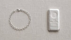 Silver bracelet and a 1-ounce .999 fine silver bullion bar side by side on a linen surface — illustrating the difference between silver jewelry and silver bullion as investments