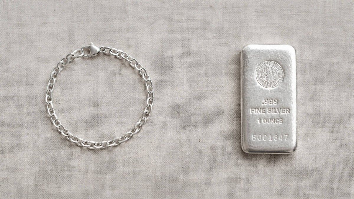 Silver bracelet and a 1-ounce .999 fine silver bullion bar side by side on a linen surface — illustrating the difference between silver jewelry and silver bullion as investments