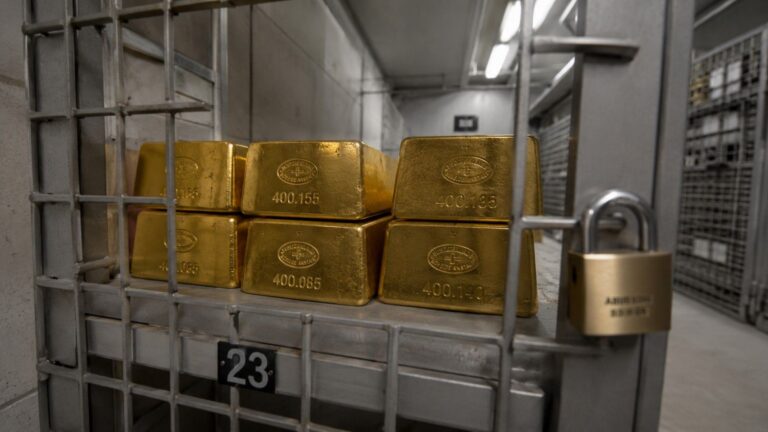 Gold bars in a numbered vault compartment, padlocked cage door marked 23, central bank gold repatriation storage