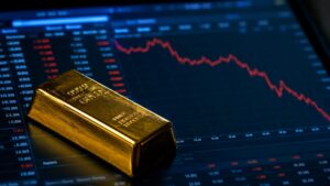 A gold bar resting on a financial screen showing a declining price chart, representing today's drop in gold prices following strong US jobless claims data.