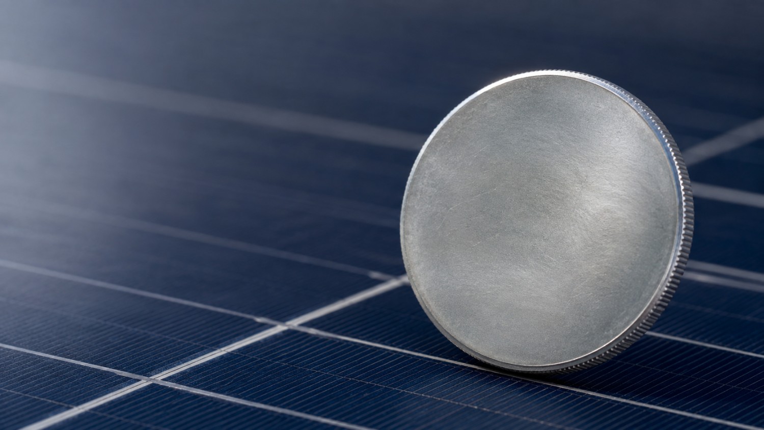 A blank silver bullion round standing on edge on a blue solar panel, the industrial demand behind why gold is down and silver is up
