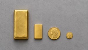 Four gold formats arranged by size on a neutral surface: a 10 oz bar, a 1 oz bar, a 1 oz sovereign coin and a 1/10 oz coin, showing why the cheapest way to buy gold depends on format.