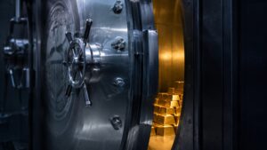 A heavy vault door standing open, revealing stacked gold bars inside, illustrating the new gold sanctions on Iran in 2026.