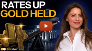 Seesaw balancing gold bars against cash and bonds in front of the Federal Reserve, titled "Rates Up, Gold Held." GoldSilver's Megan King Diaz hosts this video on gold and interest rates.