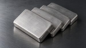 Four silver bullion bars stacked in an overlapping row on a dark brushed-steel surface, illustrating silver’s quiet retest of its 2026 low.